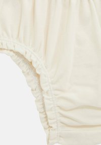 Abbigliamento in cotone color crema con bordi arricciati e una texture morbida. Presenta una vita elástica e aperture per le gambe per comfort e vestibilità.