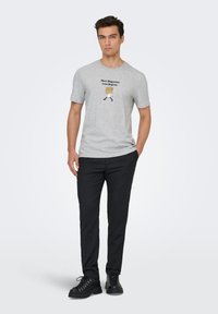 Γκρι βαμβακερό μπλουζάκι με μαύρα γραφικά κείμενα και καρτούν χαρακτήρα που κρατά μπαγκέτες. Συνδυασμένο με μαύρο παντελόνι και μαύρα παπούτσια.