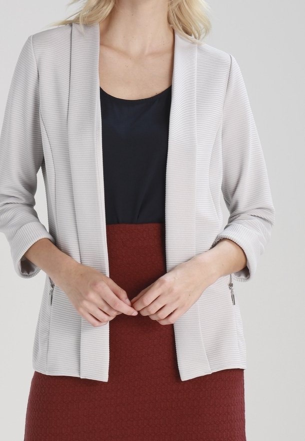 Blazer a coste grigio chiaro con apertura frontale, maniche a tre quarti e senza chiusure. Abbinato a un top blu navy e a una gonna texturizzata bordeaux.