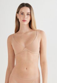 Beige, bezešvé podprsenka s tenkými ramínky a trojúhelníkovým tvarem. Měkká tkanina a jednoduchý design zdůrazňují pohodlí a minimalismus.