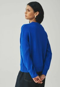 Niebieska bluza z luźnym krojem, ściągaczami w rękawach i u dołu oraz miękką fakturą. Widok z tyłu pokazuje obniżone szwy ramion i minimalistyczny design.