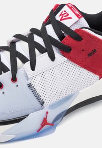 Chaussure de sport blanche et rouge avec des lacets noirs, en nubuck et matériaux synthétiques, design perforé, et logo Jumpman contouré sur la semelle.