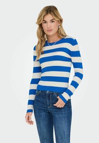Haut à manches longues à rayures bleues et blanches en rib, avec un col rond, associé à un jean en denim bleu, doté de poignets ajustés et d'une coupe décontractée.