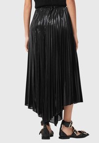 Musta laskostettu hame kiiltävällä pinnalla, jossa epäsymmetrinen helma. Yhdistetty mustiin remmikenkiin, joissa on kultaiset yksityiskohdat.