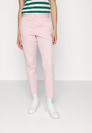 Persoon draagt lichtroze taps toelopende broek, witte sneakers en witte sokken, gecombineerd met een groen-wit gestreept shirt.