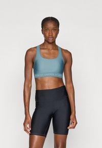 Jasnoniebieski stanik sportowy z kwadratowym dekoltem i logo Under Armour. Czarne rowerowe spodenki z wysokim stanem i detalami szwów. Gładki materiał.