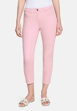 Schmal geschnittene, verkürzte pinke Hose mit Fronttaschen, getragen mit weißen Slide-Sandalen und einem weißen, eingesteckten Top.