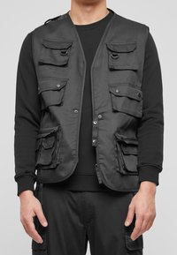 Black fabric vest featuring multiple front pockets with flaps, zippers, and snap closures, designed for utility and functionality.