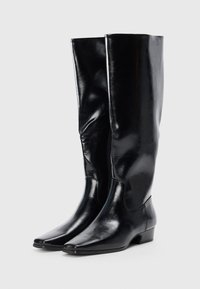 Botas negras de cuero hasta la rodilla con un acabado liso, punta afilada y tacón bajo; cuentan con una cremallera lateral para mayor comodidad al ponérselas.
