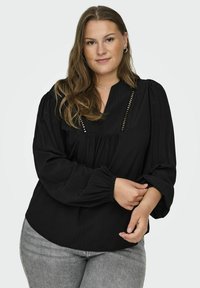Blusa nera con vestibilità rilassata, caratterizzata da una scollatura a V, dettagli plissettati e maniche a sbuffo con polsini elasticizzati. Tessuto testurizzato.