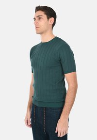 Maglione corto a maniche corte verde a coste con scollo rotondo, silhouette aderente e una texture sottile. Abbinato a jeans scuri con coulisse.
