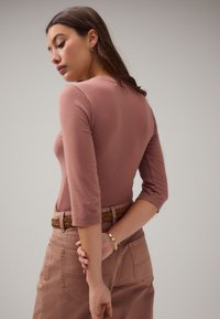 Pikkade varrukatega vormitud topp pehmest roosast ribimassist. Kombineeritud kõrge vöökohaga heledate roosade pükstega ja punutud pruuni vööga.