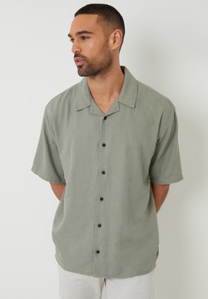 Chemise à manches courtes, verte, en tissu léger, avec une coupe décontractée, un col pointu et des boutons foncés. Texture unie.