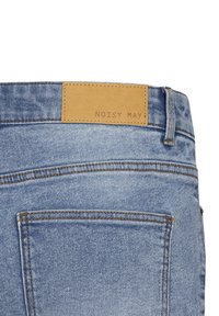 Lichtblauwe denim jeans met een tan leren label met de tekst "NOISY MAY." Heeft zichtbare stiksels en twee achterzakken.