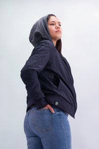 Marineblauer Bomberjacke mit grauer Kapuze, ausgestattet mit Netz-Seitenteilen, Reißverschluss und einem Logo-Patch. Kombiniert mit enganliegenden blauen Jeans.