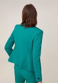 Turkusowa marynarka dopasowana w sylwetce, z gładkiego materiału, z detalem pojedynczego guzika przy mankiecie. Posiada rozcięcie z tyłu dla większej swobody.