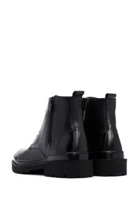 Botas de tobillo de cuero negro con una textura suave, cordones en la parte delantera y cremalleras laterales, con una suela de goma gruesa.