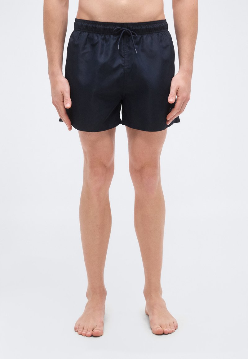 Μπλε ναυτικό μαγιό σορτς από ελαφρύ ύφασμα που στεγνώνει γρήγορα. Διαθέτει ελαστική μέση με κορδόνι, πλαϊνές σκισμές και ομαλή υφή.