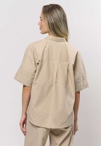 Beige kortärmad skjorta i lätt tyg med avslappnad passform, bakre veck och klassisk krage.