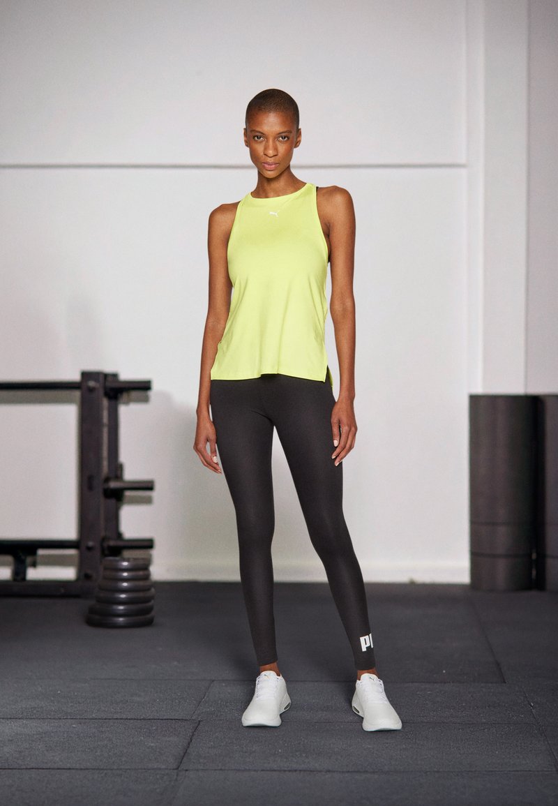 Top da ginnastica senza maniche verde lime e leggings neri, abbinati a scarpe da ginnastica bianche; design pulito con dettagli del logo sui leggings.