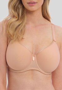 Světlý béžový podprsenka s hladkými košíčky, nastavitelné ramínka a malou dekorativní detalí v centru. Měkká textura a jemný lem podél okrajů.