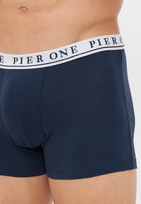 Tamnoplave bokserice izrađene od mekanog, rastezljivog materijala; imaju bijeli pojas s logom "PIER ONE" u tamnom slovlju.