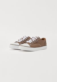 Zapatillas de lona marrón con cordones blancos, punta de goma y suela blanca. Entre sus características se incluyen costuras en contraste y un pequeño detalle de logo.