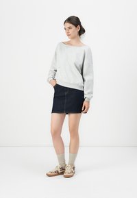 Felpa grigia, oversize, con scollatura ampia, abbinata a una mini gonna in denim scuro. Scarpe color tan con stampa e calzini beige chiaro completano l'outfit.