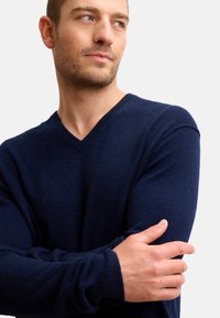 Marinblå v-ringad tröja i mjukt material, med långa ärmar och en tight passform. Minimalistisk design utan synliga mönster eller detaljer.