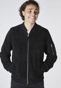 Svart mockabomberjacka med dragkedjestängning, ribbade ärmslut och en ficka på vänster ärm. Slät textur och minimalistisk design.