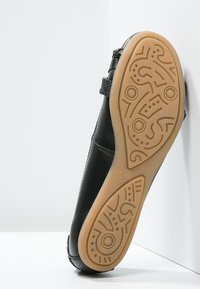 Scarpa nera in pelle con suola flessibile, caratterizzata da una suola decorata con un motivo intricato e una parte superiore liscia. Include dettagli con cinghie per una vestibilità sicura.