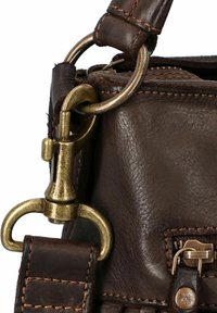 Hoek van een bruin leren tas met zichtbare stiksels, metalen hardware en een sluiting. Heeft een rits en een gestructureerde afwerking.