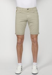 Bermudas de algodón color caqui con puños doblados, cinco bolsillos y herrajes metálicos. Llevadas con zapatillas blancas y calcetines hasta el tobillo.