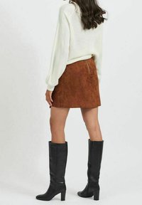 Brown suede mini skirt with a back zipper, paired with a white knitted sweater and black knee-high boots, creating a layered look.