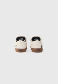 Kaks tükki off-white madalate tossude paar, pruunide talladega, vaadatuna tagant, näidates iga kanna peal "etnies" logo.