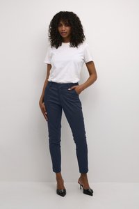 Marineblaue, taillierte Hose mit seitlichen Taschen, kombiniert mit einem schlichten weißen T-Shirt. Modell trägt schwarze spitze Absatzschuhe. Glatte Textur, schlanke Silhouette.