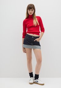 Rode geribbelde coltrui, donker denim minirok met lichtgewassen zoom, witte sneakers met marineblauwe accenten en zwarte sokken.