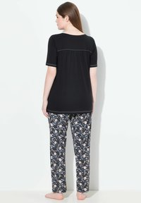 Svart kortärmad topp med rynkad baksida; ihop med mönstrade pyjamasbyxor i mörkblått och krämfärgad blommönster. Mjuk tyg.