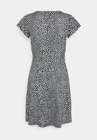 Robe noire à manches courtes avec des pois blancs, taille cintrée et jupe évasée, vue de dos sur fond uni.