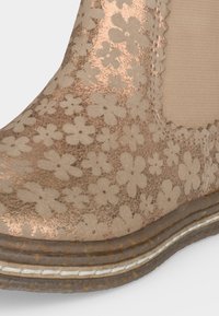 Gros plan d'une botte beige et marron à la cheville avec un motif floral et une semelle épaisse avec un détail de couture blanche.