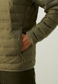 Olivengrønn dunjakke med horisontale quiltede seksjoner, en glidelåslomme og elastiske mansjetter, med en glatt, lett skinnende tekstur.