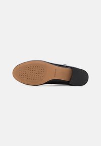 Chaussure en cuir noir avec un bout arrondi et une semelle en caoutchouc flexible. Le dessous présente un motif perforé pour la respirabilité.