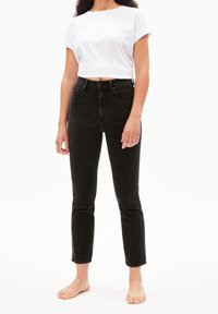 Černé džínsy s vysokým pasem a úzkým střihem, zkrácené nad kotníky. Kombinované s bílým tričkem s kulatým výstřihem. Minimalistický design, žádné viditelné vzory.