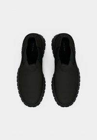 Sorte slip-on sko med en glatt, matt overflate, rund tå og strukturert gummisåle. Minimalistisk design uten synlige detaljer.