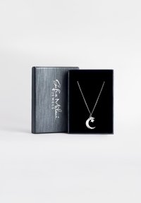 Srebrny naszyjnik z zawieszką w kształcie crescenta, umieszczony na delikatnym łańcuszku, wyeksponowany w czarnej pudełku wyłożonym aksamitem, o eleganckim szarym wykończeniu.