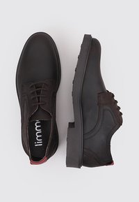 Zapatos de vestir de cuero marrón con un acabado suave, puntera redonda, diseño de cordones y una suela de goma negra contrastante. Presenta detalles de costura sutiles.