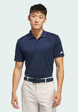 Marineblauw poloshirt met een kraagontwerp en drie knopen, gecombineerd met witte broek en een gestructureerde blauwe riem. Inclusief het Adidas-logo op de mouw.