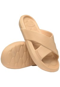 Light beige slide sandals made of soft rubber with a cross-strap design and textured footbed, featuring a patterned sole for grip.