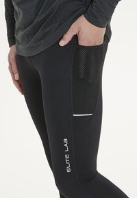 Sorte atletiske leggings har en mesh-lomme, hvide detaljer og en tætsiddende pasform. Lavet af strækbart materiale, velegnet til sportstøj.