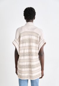 Beiger Strickpullover mit weit geschnittenen Ärmeln, der über strukturierte Streifen und ein offenes Webmuster verfügt. Hoher Kragen und klare Knopfdetails auf der Rückseite.